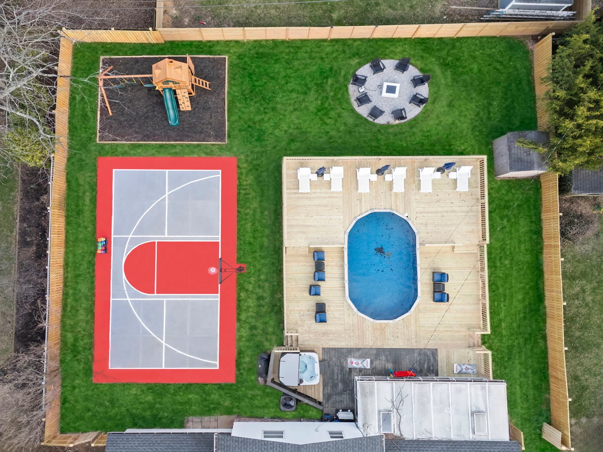 Aerial view of a backyard featuring a small basketball court, a wooden play structure with a slide and a swimming pool
