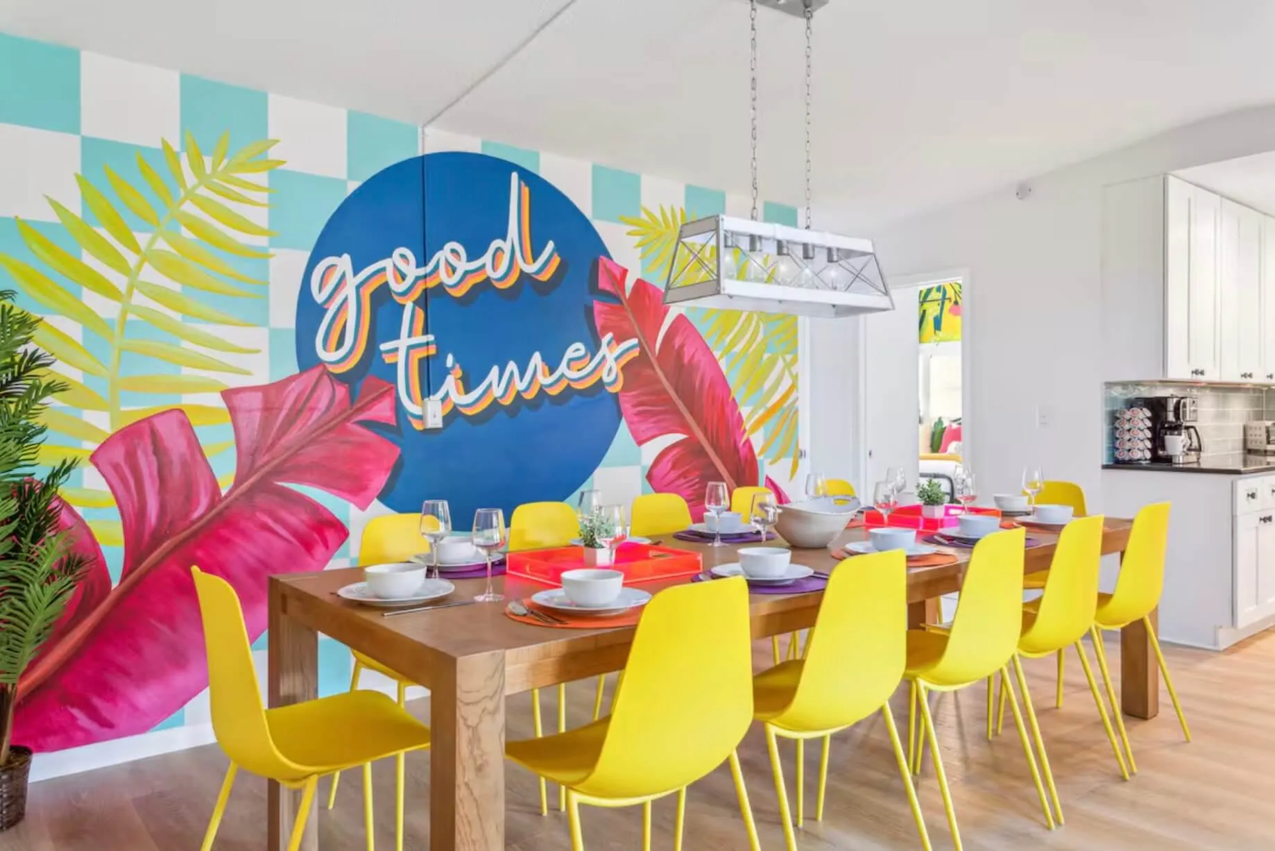 Dining room with a large wooden table set, surrounded by bright yellow chairs and a colorful mural on the wall.