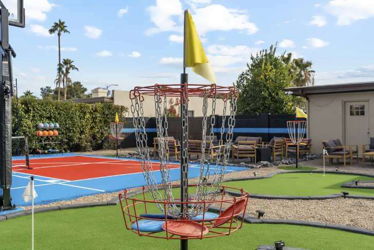 Outdoor recreational area featuring a disc golf basket with chains and a yellow flag.